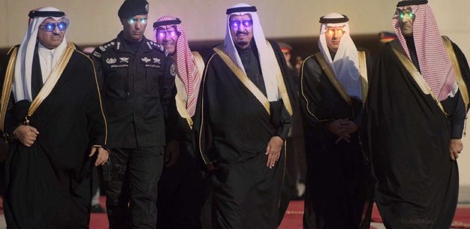 Several men in traditional Saudi attire, including white thobes and red-checkered ghutras, walk together wearing futuristic AR/VR glasses, with one individual in a dark military uniform. The image evokes Saudi Arabia's technological modernization, which aligns with the post promoting giveaways for "The Saudis NFT" project and its associated social channels.
