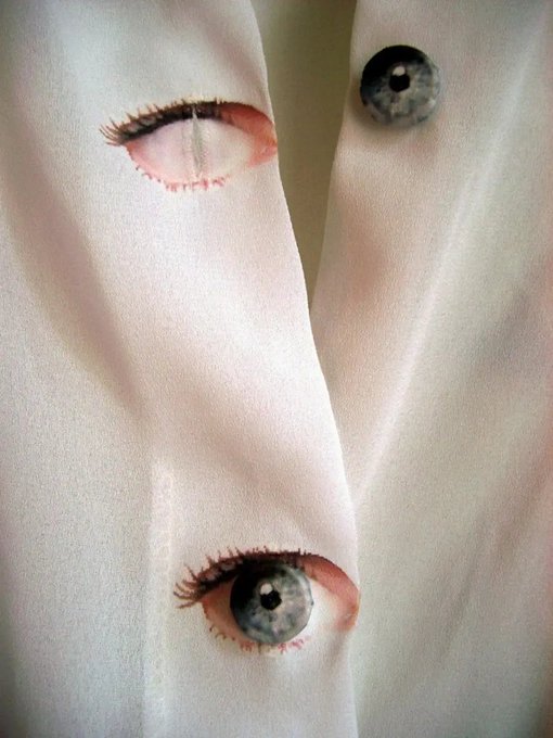 A close-up of white fabric featuring realistic painted eyes with blue irises and eyelashes, alongside a separate button-like eye.
