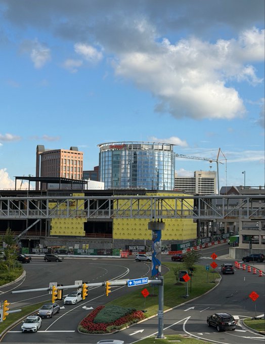 An urban street scene featuring a Marriott hotel, a large yellow building, an elevated walkway, and an intersection labeled 'Tyson Blvd' with cars and construction cranes.