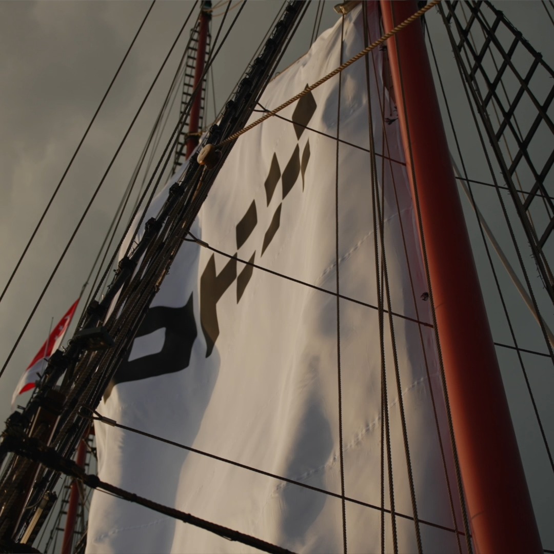 A tall white sail billows in the wind on a ship's mast, with the word "OKX" prominently displayed in black lettering. The image evokes themes of adventure and partnership, fitting the post's celebration of VIP guests joining OKX in Singapore for collaborative product discussions and networking.