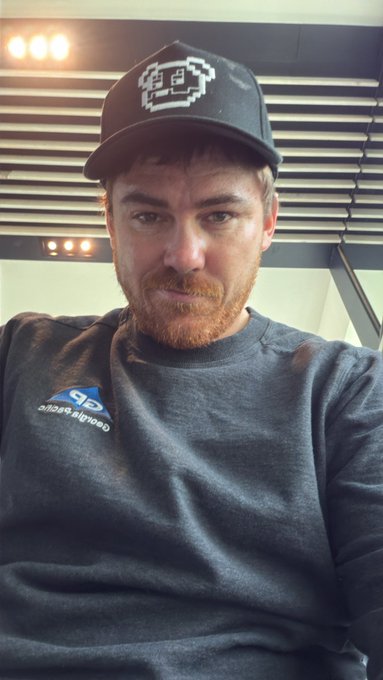 A selfie of a bearded man wearing a black baseball cap with a pixel-art face logo and a dark grey sweatshirt featuring a 'CentrePort Canada' logo with the number 45.