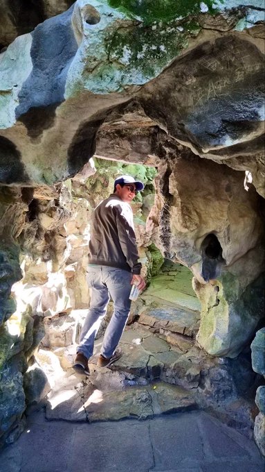 A man in a cap, jacket, and jeans explores a rocky, cave-like structure with stone steps, likely during a sightseeing excursion in Shanghai as part of the Solana Capital Forum trip to China.