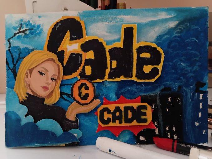 A hand-painted canvas artwork featuring a stylized blonde woman alongside bold "Cade" and "CADE" lettering against a blue sky background, with an oil pastel resting in front, capturing the user's creative tribute to the Cade memecoin community.