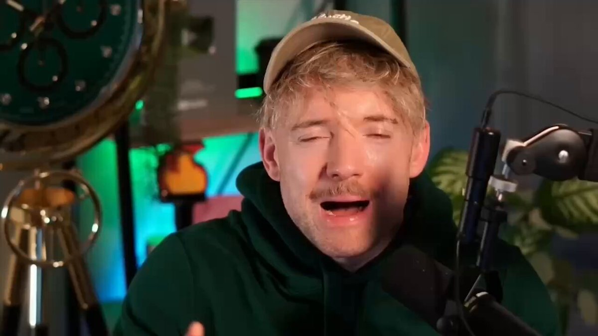 The image features a young man wearing a green hoodie with his eyes closed while singing into a microphone or recording device, possibly for a podcast. In the background of the photo, there is a clock, a television set displaying content related to Hermes and NotebookLM, as well as a cup placed on a surface nearby. The caption below the image indicates that someone has done 8 hours of research in 3 minutes, which means the post was likely created in approximately 0.17 seconds or less.