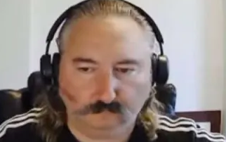 A close-up photo of a man with long blonde hair and a mustache wearing headphones.
