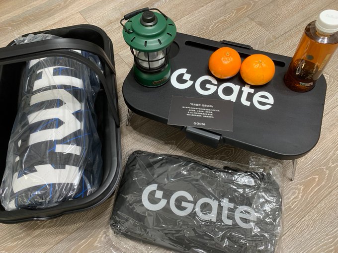 A promotional or travel kit featuring GGate branded merchandise including a luggage bag, folding table, lantern, oranges, tea, and a clothing item in plastic packaging.