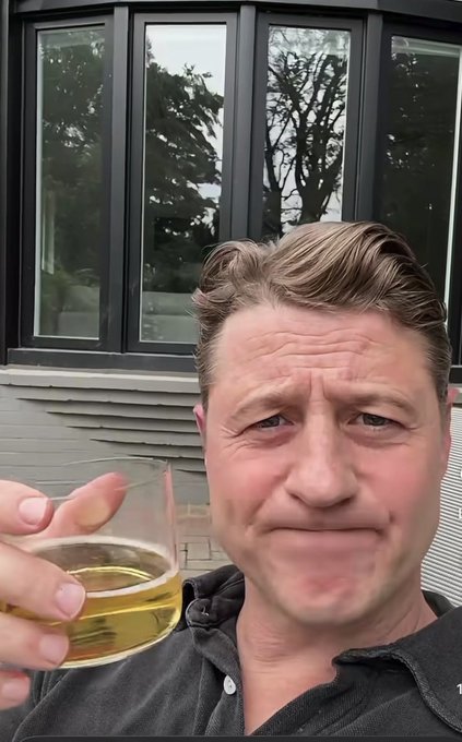 A man raises a glass of amber liquid, appearing to celebrate a downturn in Bitcoin's 4-year cycle, as indicated by the text and ticker $BTC in the accompanying post.