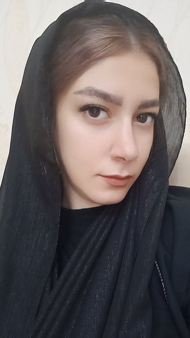 A close-up selfie of a woman wearing a black hijab, with neat arched eyebrows and a serene expression.