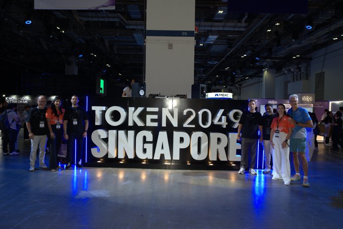 A group of people posing for a photo in front of a large illuminated 'TOKEN 2049 SINGAPORE' sign at what appears to be a crypto conference.