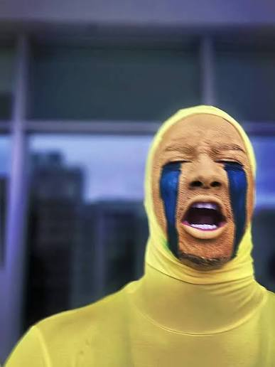 A person wearing a yellow bodysuit and balaclava with blue face paint mimicking crying eyes stands with an open-mouthed, exasperated expression, perfectly embodying the post's disbelief about the undervaluation of $SOB relative to other NFT collections. The image visually conveys the "crying" meme sentiment used in the accompanying caption to critique the market's illogical pricing.