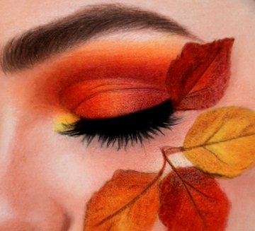 A close-up of a closed eye with warm orange and red eyeshadow, decorated with autumn leaves in red and yellow tones placed on and around the eye.