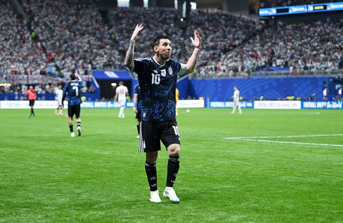 Lionel Messi, wearing the Argentina national team jersey with the number 10, raises his arms in celebration on the soccer field, embodying the "AURA" of his legendary presence and skill.