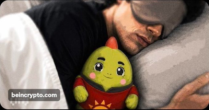 A photograph of a man sleeping while hugging a plush toy of the BeInCrypto mascot, a green avocado-like character wearing a red shirt, with a 'beincrypto.com' watermark in the corner.