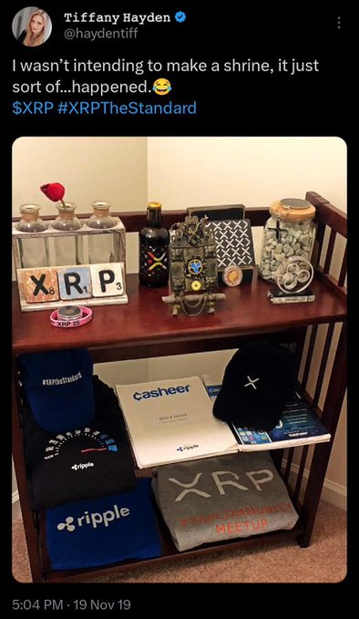 A tweet from Tiffany Hayden (@haydentiff) shows a wooden table turned into an XRP-themed display, featuring XRP-branded apparel, a Casheer book, a Ripple hat, and decorative items with scrabble tiles spelling "XRP." The caption reads "I wasn't intending to make a shrine, it just sort of...happened😅 $XRP #XRPTheStandard," tying into the post's reference to "XRP 813" as part of her XRP fan collection.