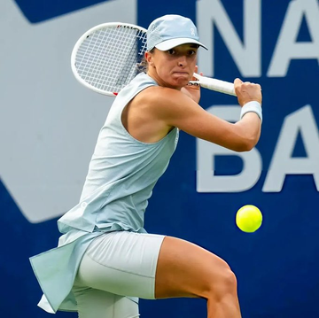 A female tennis player wearing a white outfit and cap swings a racket at a tennis ball during a match.