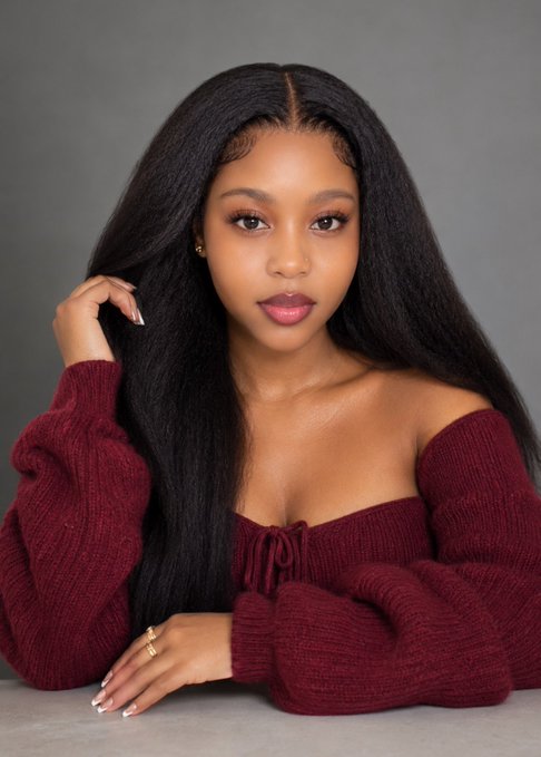 A portrait of a young woman with long, straight black hair wearing a burgundy off-the-shoulder ribbed sweater.