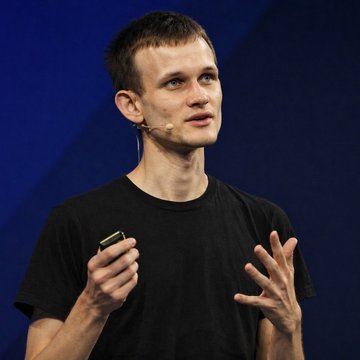 A young man with short hair wearing a black t-shirt and a headset microphone speaks while gesturing with his hands against a dark blue background, appearing to be giving a presentation. The image likely depicts Vitalik Buterin, Ethereum's co-founder, delivering the talk referenced in the caption about cryptocurrency's resilience in the AI era.