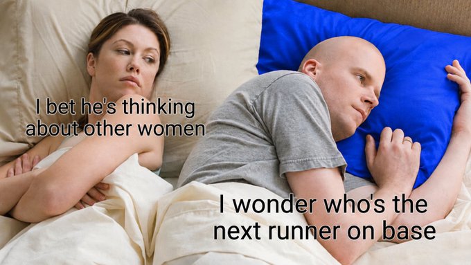 A couple lies in bed facing away from each other, with the woman captioned "I bet he's thinking about other women" and the man captioned "I wonder who's the next runner on base," humorously contrasting her romantic insecurity with his distraction over baseball.