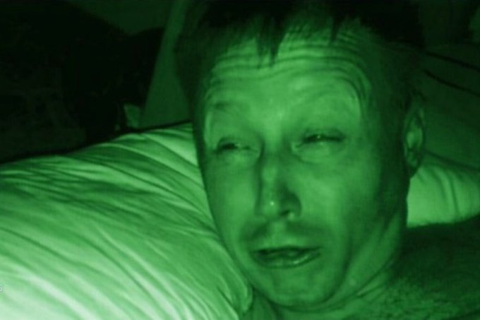 A grainy, night-vision style green-tinted close-up photo of a man's face resting against a striped pillow.