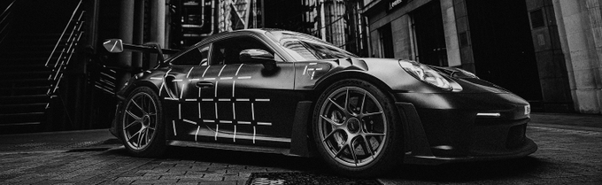 A sleek black sports car, resembling a Porsche 911 GT3, parked in an urban alleyway with a grid pattern graphic on its side.