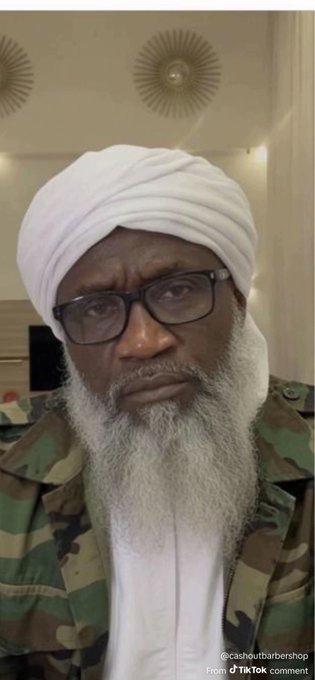 A man with a white turban, long white beard, and glasses wearing a camouflage jacket, posted by @cashoutbarbershop on TikTok.