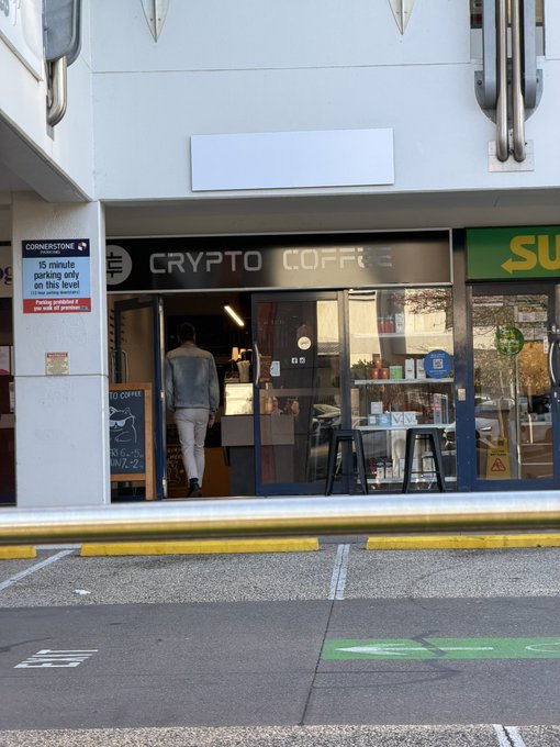A street-level view shows a man entering "Crypto Coffee," a shop with large glass windows, next to a Subway restaurant and a parking sign indicating "15 minute parking only."