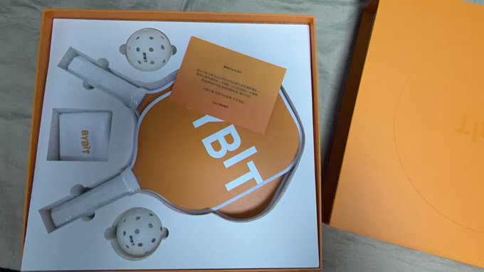 An open orange box containing orange BYBIT-branded headphones and an informational card.