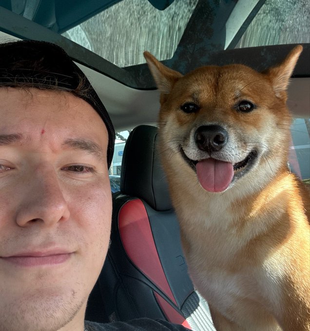 A man takes a selfie inside a car with his happy-looking Shiba Inu dog (Leo) sitting in the passenger seat with its tongue out. The post humorously suggests Leo the dog is giving bullish crypto advice about Solana reaching $500.