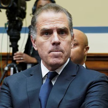 Hunter Biden, dressed in a dark suit and blue tie, sits with a stern expression during what appears to be a congressional hearing. The image accompanies news about Hunter Biden's plea to Elon Musk to restore a cryptocurrency account tied to his infamous laptop, which has since plummeted in value by 99.3%.