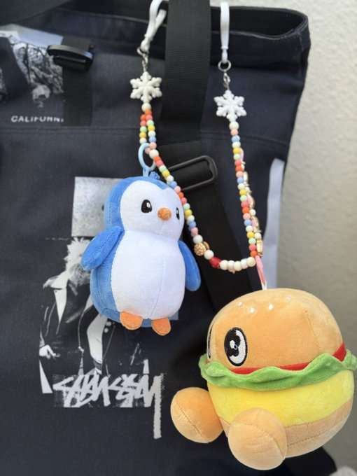 A black tote bag with 'CALIFURN' text and a Stüssy logo, decorated with plush keychains including a penguin and a hamburger character on beaded straps.
