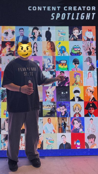A person wearing a black 'FEAR OF GOD' shirt and gray pants stands in front of a 'CONTENT CREATOR SPOTLIGHT' wall covered in a grid of various digital avatars and photos.