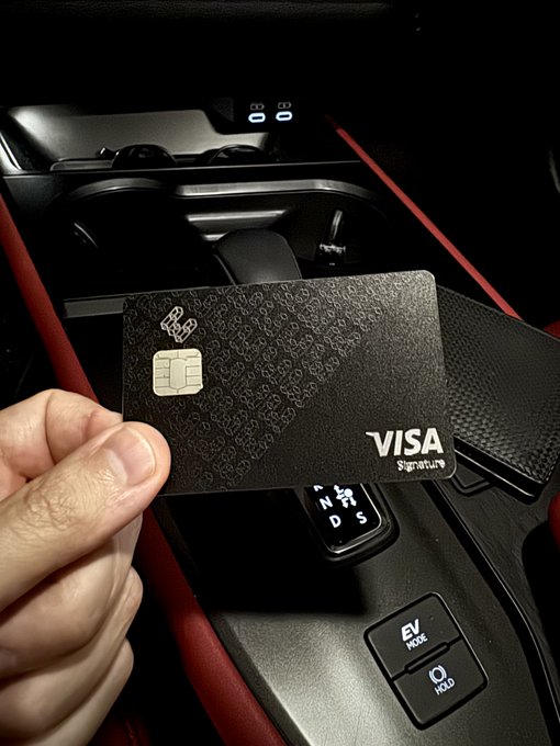 A hand holds up a sleek black Visa Signature credit card inside a car, showcasing the integration of crypto-native banking into everyday luxury, as highlighted in the EtherFi user guide. The visible "EV MODE" and "HOLD" buttons on the center console add a futuristic touch that complements the post's theme of modern, multi-functional financial tools.