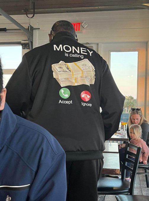 A person wears a black jacket on their back that reads 'MONEY is calling' above an image of cash and phone buttons labeled 'Accept' and 'Ignore', with a young girl visible in the background.