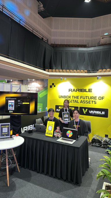 A team of three staff members pose at the "RARIBLE - UNBOX THE FUTURE OF DIGITAL ASSETS" booth at Malaysia Blockchain Week, displaying tablets, a QR code, and what appears to be a prize pack, offering attendees a chance to win digital collectibles in keeping with the "crack a pack" giveaway promotion.