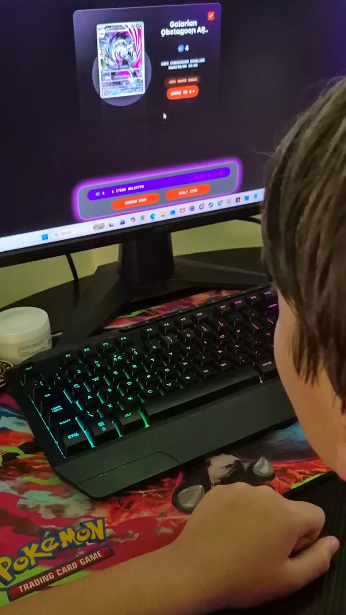 The image shows a person playing a video game using a computer monitor with a keyboard and mouse. The person appears to be focused on their gameplay, likely enjoying the Pokémon Go game displayed on the screen.