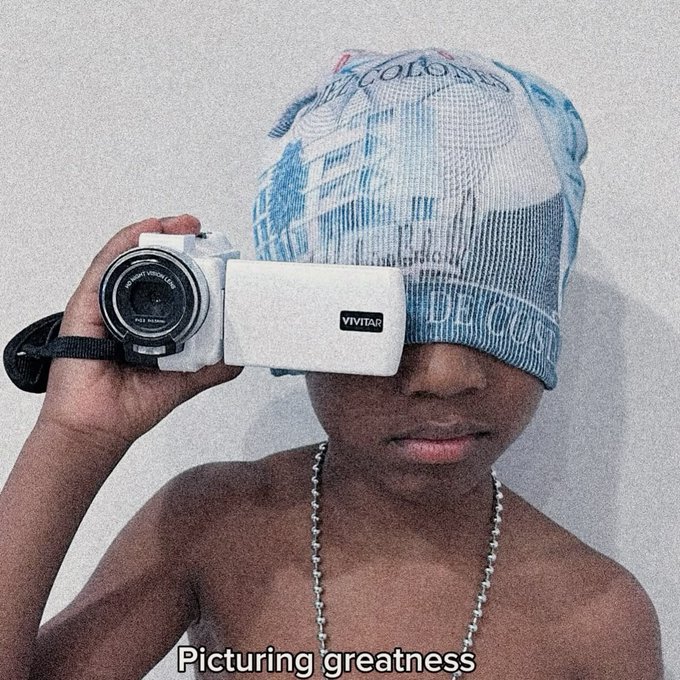 A shirtless person wears a mesh trucker cap printed to look like a blue $100 bill over their eyes, holding a white Vivitar camcorder up as if filming, with the caption "Picturing greatness" below.

The image plays on the "good morning" post by framing the videographer—money literally covering their vision—as someone "picturing greatness" first thing in the morning.