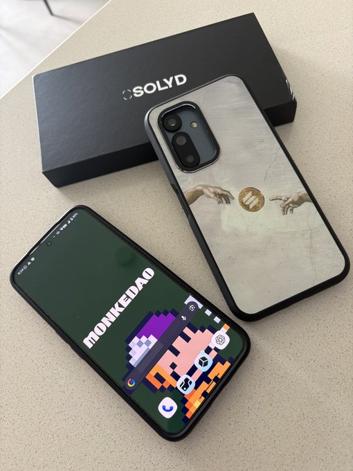 Two Solana phones with Seek ($SKR) branding are displayed—one showing the "MONKEDAO" wallpaper with pixel art on screen, and the other featuring the iconic Creation of Adam hands with the Seek logo as the centerpiece. The Solyd packaging box sits in the background, reinforcing the post's showcase of Seeker devices.