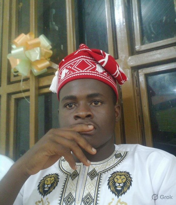A selfie of a man wearing a red and white patterned traditional cap and a white embroidered shirt with lion motifs, posing thoughtfully with his hand near his mouth, watermarked with 'Grok'.