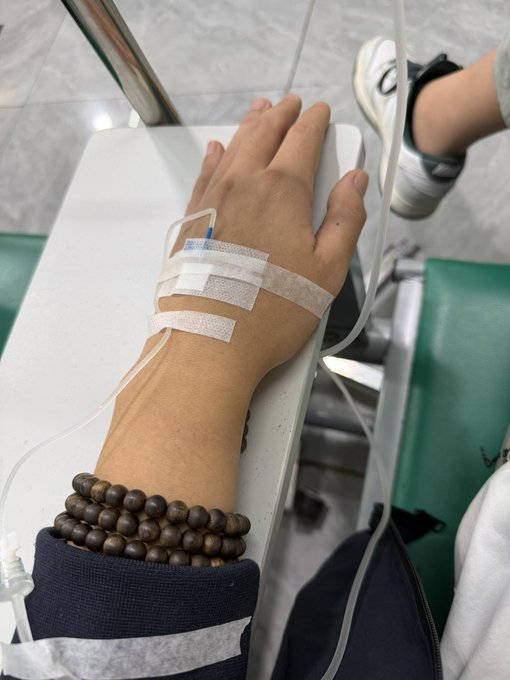 A person's hand rests on a hospital chair with an IV line taped to it, while their other foot is propped up wearing a white sneaker. The image suggests the poster is currently at a medical facility for IV treatment, with the context hinting that the dental pain from their wisdom tooth may be severe enough to require medical attention beyond a standard ibuprofen remedy.