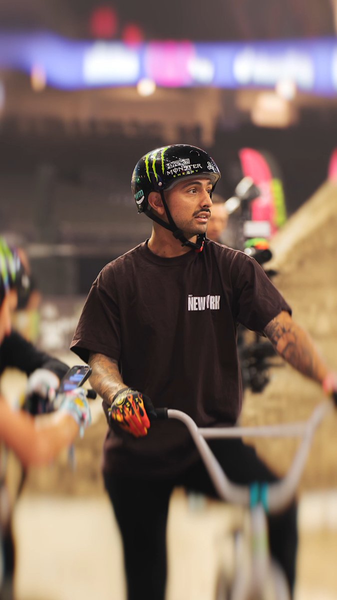 A BMX rider wearing a "NEW YORK" shirt and a Monster Energy-sponsored helmet stands with his bike at an indoor arena. The image ties to the post about the New York team competing in the @moonpay X Games League 2026 Summer Championship with 1770 points.