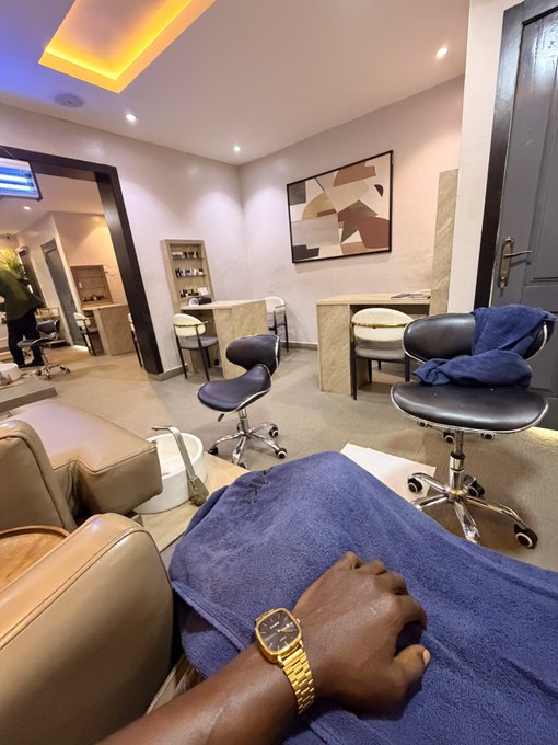 A first-person view from a salon chair shows a man wearing a gold watch, relaxed in a luxurious barbershop with modern decor and mirrors. The image complements the post by depicting a well-deserved moment of pampering, suggesting the reward of staying strong through crypto's volatile bear market.