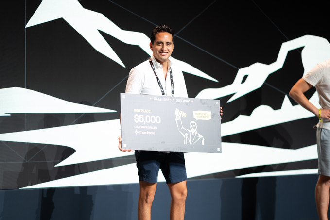 A smiling man on stage holds a large novelty check displaying '85,000 USD' alongside tokens at the Token 2049 Dubai event.