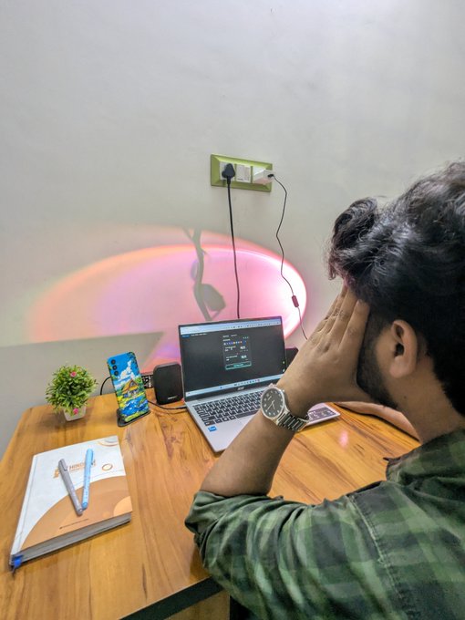 A young man sits at a wooden desk working on a laptop displaying what appears to be video editing software, with a smartphone, notebook, and a pink ambient sunset lamp illuminating the workspace. The scene reflects the post's message of a 21-year-old video content creator, showcasing his creative setup as a creator for @binance and @P2Pdotme.
