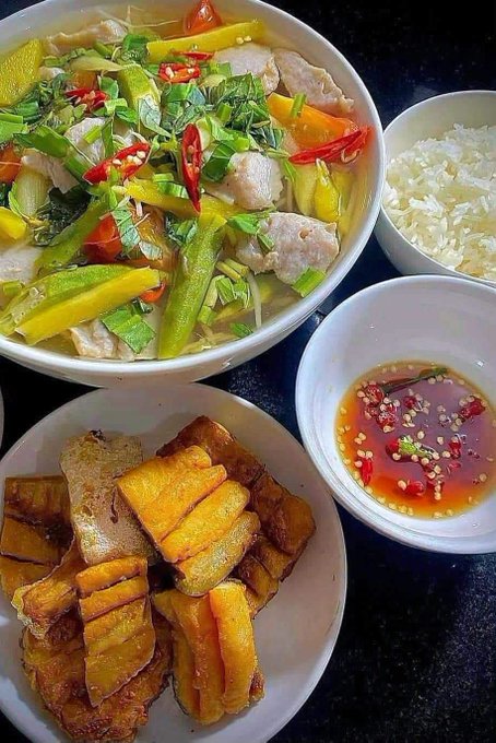 An overhead view of a Vietnamese meal with a bowl of fish and vegetable soup, white rice, fried tofu, and a small bowl of fish sauce with chili.