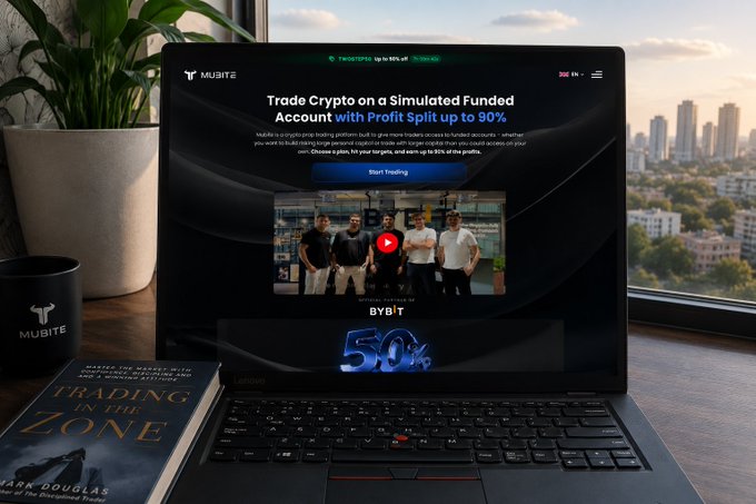 A laptop on a desk displaying the Mubite website with the headline 'Trade Crypto on a Simulated Funded Account with Profit Split up to 90%,' showing a YouTube video and a 'BYBIT 50%' graphic.