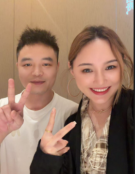 A man and a woman smile together for a selfie, both flashing peace signs, with the man in a white shirt and the woman in a patterned top and large hoop earrings, capturing the friendly and warm first-meeting moment referenced in the accompanying post.
