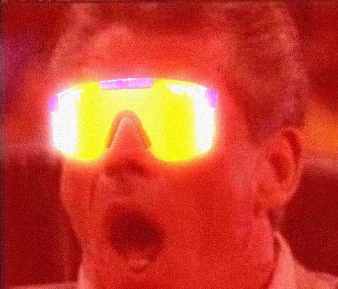 A heavily filtered, red-tinted close-up photo of a man wearing large reflective yellow sunglasses with an open-mouthed expression.