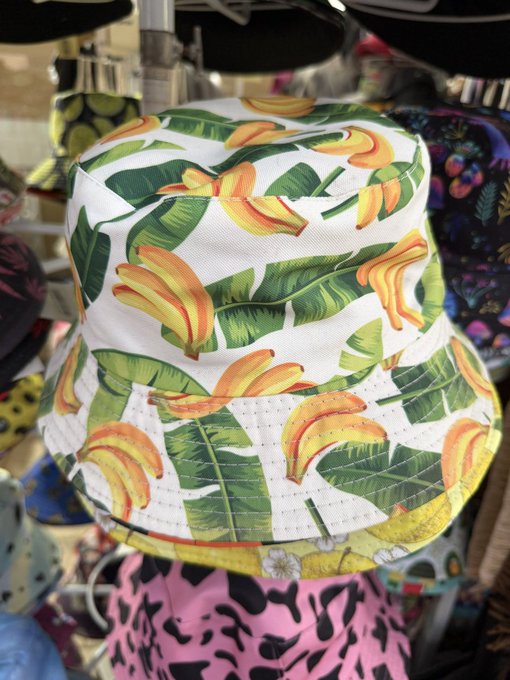 A bucket hat featuring a tropical pattern of bananas and green leaves on a white background, displayed among other colorful hats.