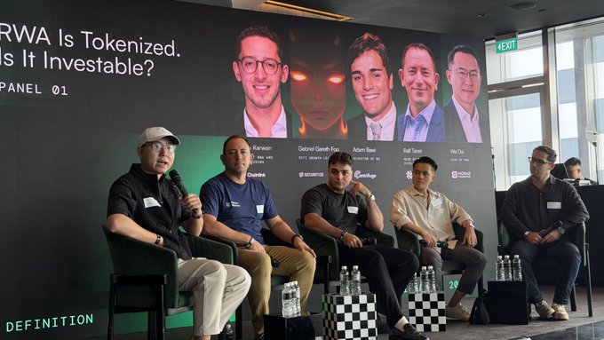 A panel of five men sit on stage discussing 'RWA Is Tokenized. Is It Investable? Panel 01', with their names and companies displayed on the screen behind them, including Gabriel Tan from Decentral and Rai Taran from Wazir Advisors.