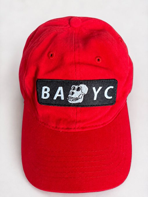 The image features a red baseball cap with a white skull design on the front, positioned against a plain gray background. The hat has a "BAYC" patch on the side, which could be a logo or an advertisement for a product or service related to BAYC.